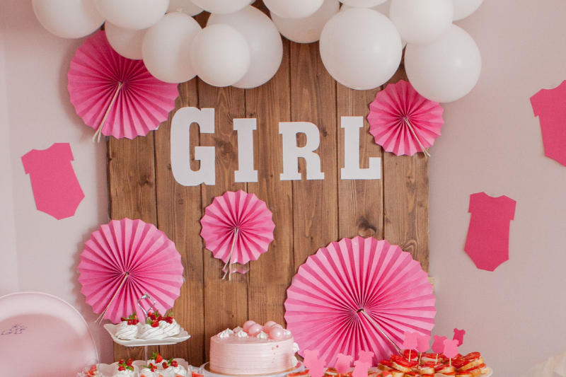 GIRL baby shower decorations with white balloons, pink fans, pink onesie cutouts, cakes.